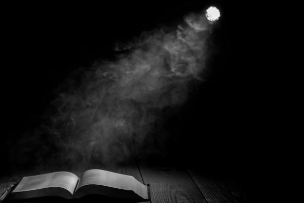 Dark image with a beam of light from a spotlight shining on an open book