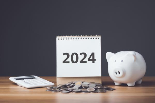 Calendar reading 2024 on desk alongside calculator, piggy bank and coins