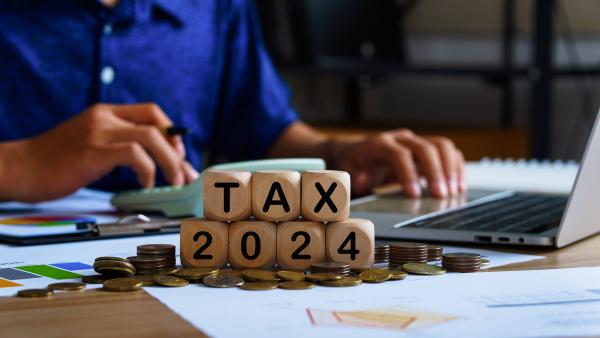 Wooden blocks reading "Tax 2024" on desk with person working in the background