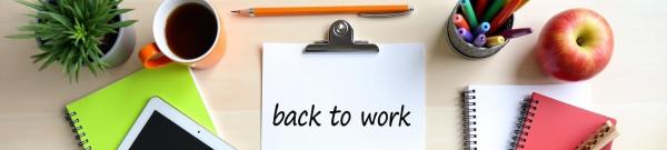 Close up of a desk with stationery and books, a clipboard in the centre with a paper and the words 'back to work' on it