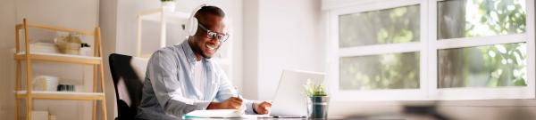 Image shows a man wearing headphones and working on a laptop at a desk