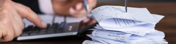 Pile of receipts on a desk with hands using a calculator and completing a form