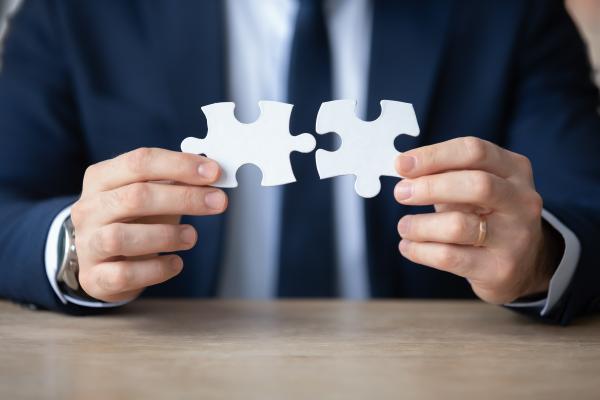 Man in suit holding a large jigsaw piece in each hand, which fit together perfectly