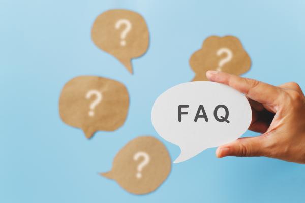 Image showing questions marks in the background and a hand holding a speech bubble with the word FAQ in the foreground