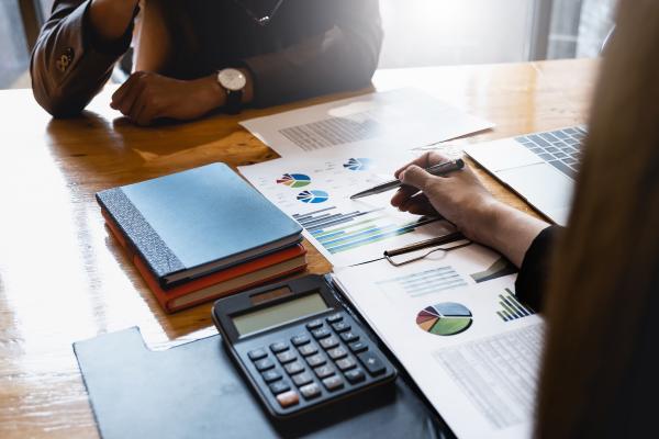 A desk with calculator and budget papers, and two people either side