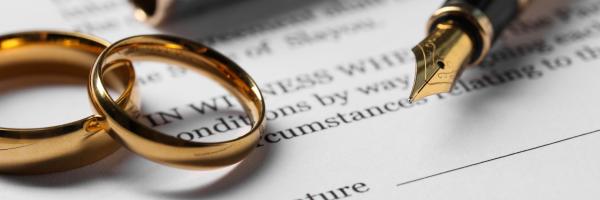 Two gold wedding rings laid on top of a marriage contract with a fountain pen nib to the right