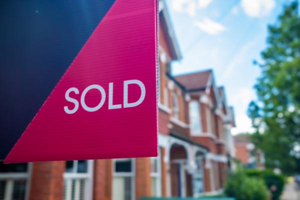 Row of brick houses in background, with estate agent's sign in foreground reading "Sold"