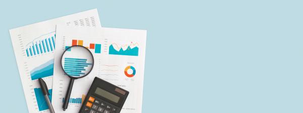 Charts and graphs on two pieces of paper with a calculator, pen, and magnifying glass, on a plain blue background