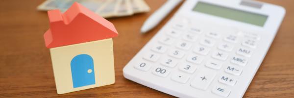 Image shows a small wooden blocks house next to a calculator