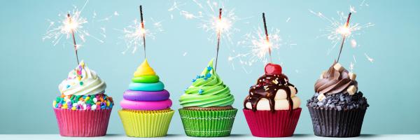 Image shows a row of colourful cupcakes and icing each with a sparkler