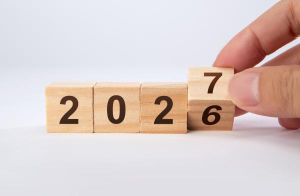 Wooden blocks reading 2026 with a hand turning the "6" over to become a "7"