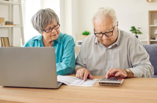 Two older people sat at a table using laptop and calculator
