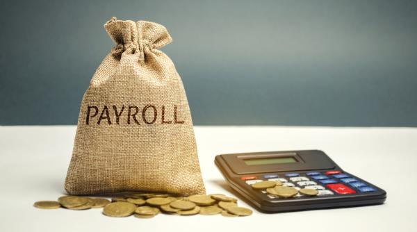 A bag of money marked payroll sits on a desk next to a calculator