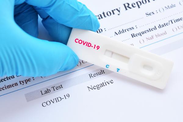 A blue gloved hand holds a negative covid test in front of a document confirming the result