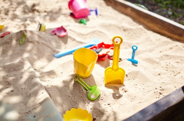 A selection of plastic toys lying in dappled light strewn across the corner of a sandpit