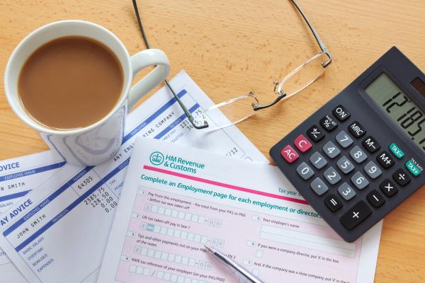 Paper tax return on a desk next to calculator and mug of tea