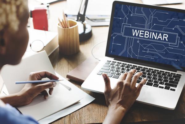 Woman sat at desk using laptop with the word Webinar on screen