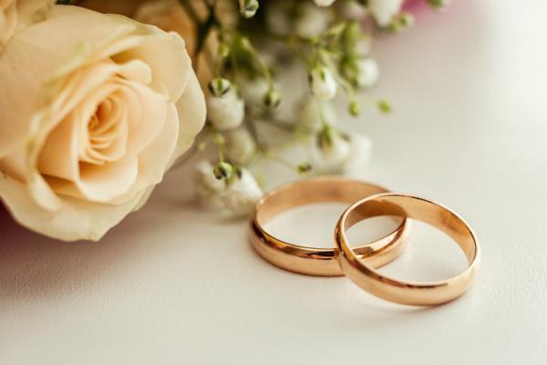 Two wedding rings overlapping on a table next to a rose and other flowers