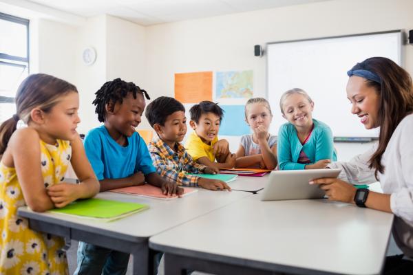 Teacher giving children sat around a table a lesson using a tablet computer