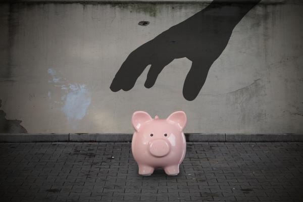 Piggy bank with a menacing hand hovering above it