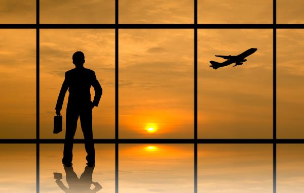 Man in business clothes stood at airport window watching aeroplane take off