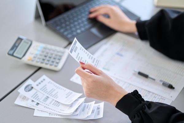 Person using laptop at a desk, holding receipts with paperwork and calculator on desk