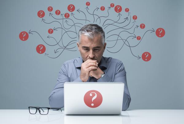 Man sat behind laptop looking thoughtful and surrounded by question marks