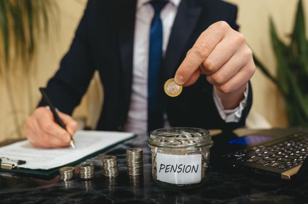 Man in suit doing paperwork at a desk and adding individual coins into a jar from piles of coins infront of him