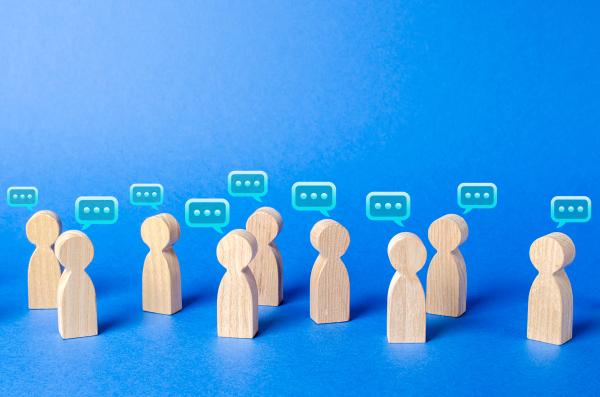 A group of wooden toys symbolising people are standing around on a blue background with little speech bubbles above to show a group in conversation 