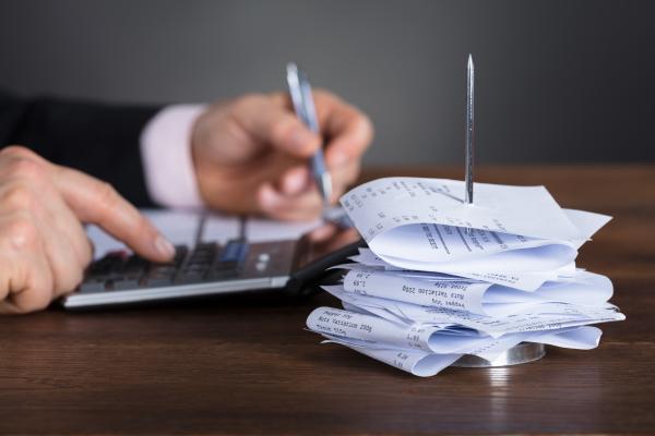 Pile of receipts on a desk with hands using a calculator and completing a form