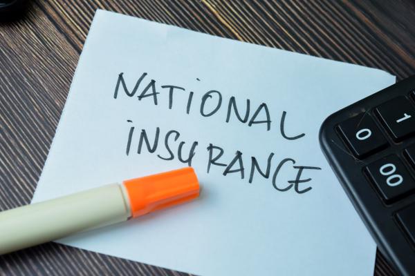 A white piece of paper with the words 'national insurance' written in capitals is lying on a desk with a pen and calculator
