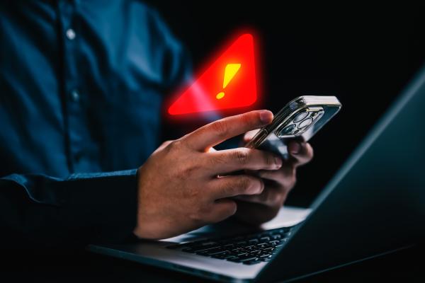Man using mobile phone and laptop with a superimposed red exclamation mark warning symbol