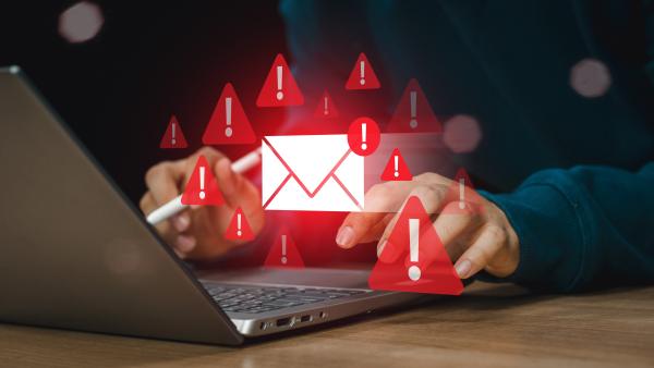A red email icon and red triangular warning signs hover in the air over a man about to type into his laptop