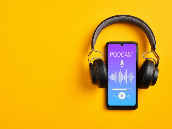 Listening podcast with smartphone player app. Smartphone and wireless headphone with podcast screen on yellow background.