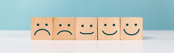 Five wooden block lined up with simple faces drawn, ranging from smiling at one end to increasingly unhappy faces at the other