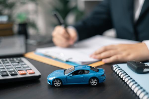Close up of someone signing paperwork on a desk with a calculator and model car on it,