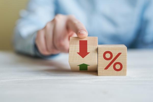 Two wooden blocks on desk - one showing % sign, the other shows up arrow on one side, down arrow on the other and is being flipped between the two by a man's hand