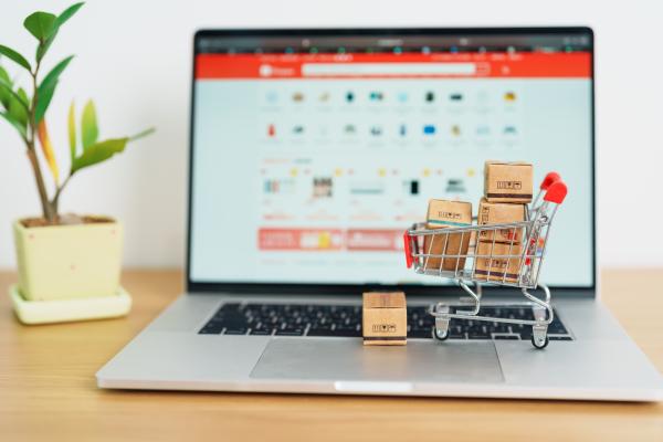 Laptop on a desk with a miniature shopping trolley filled with parcels on top of it