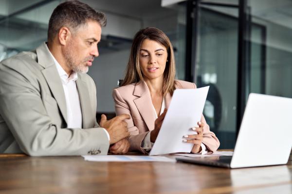 Man and woman in meeting room looking at papers with a laptop on the desk