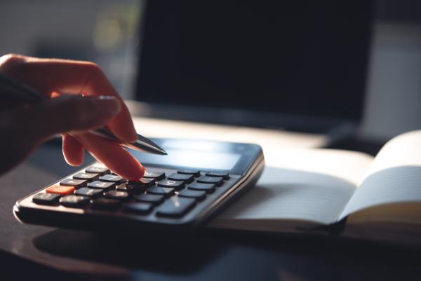 Calculator and book on a desk, with a close of person's hand using the calculator