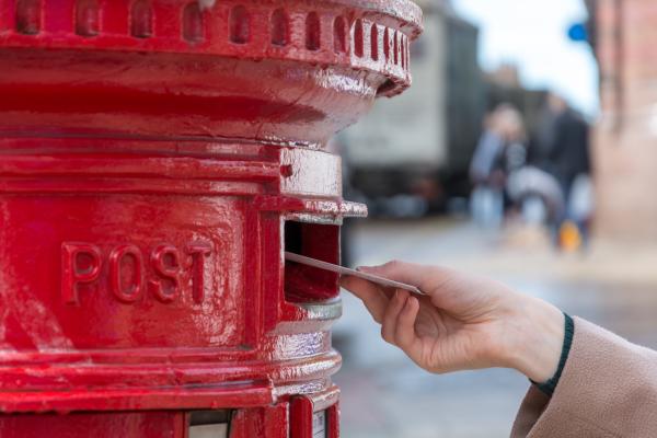 Close up of red Royal Mail post box with a hand posting a letter into it