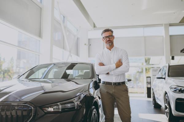 Smartly dressed man stood in car showroom between two new cars