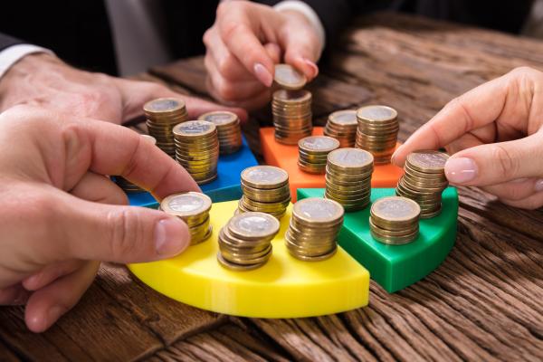 Piles of coins stacked on quarters of a coloured pie chart with hands reaching for the coins
