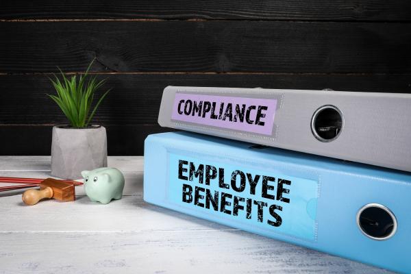 Two ring binder files on a desk - one labelled "Compliance", one "Employee Benefits"