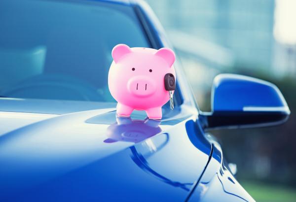 Pink piggy bank with a car key fixed to it, resting on a car bonnet 