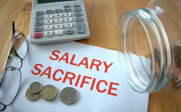 Paper on a desk with "salary sacrifice" written on it, surrounded by coins, coin jar, glasses and a calculator