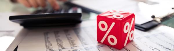 Red cube with percentage signs resting on data printout next to calculator 