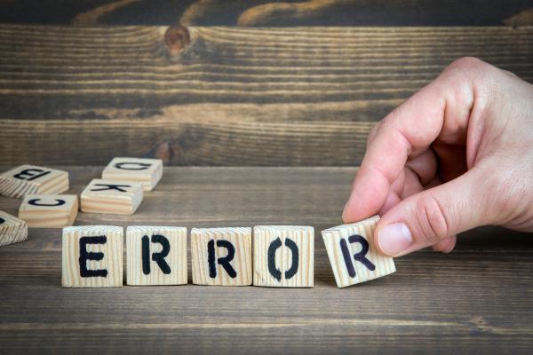 A set of wooden letters spelling out the word error are sitting on a wooden table. A hand is adding the final 'r' to the row. 