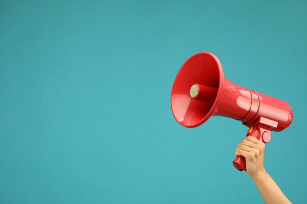 A woman holds up a large red megaphone against a teal background.