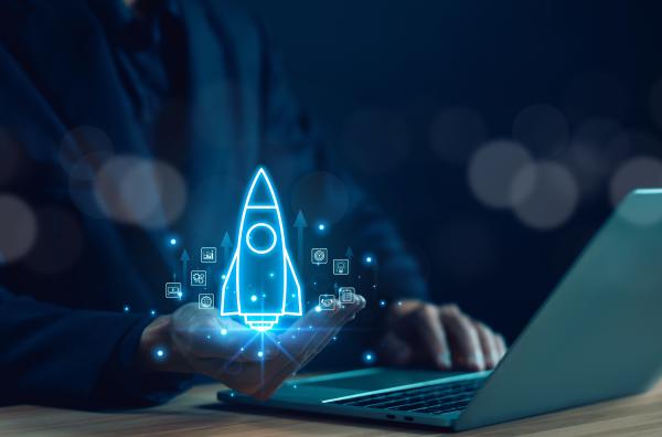 Image shows a person using laptop on desk with a bright digital projection of a space rocket launching